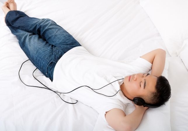 Hombre acostado con audífonos aprendiendo inglés mientras duerme